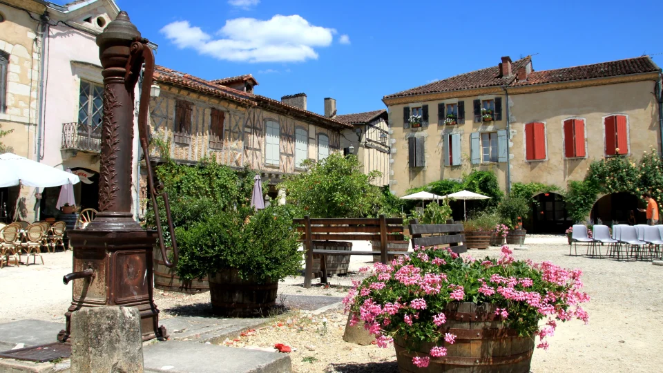 Charming town square in Labastide-d'Armagnac, France, featuring a historic water pump, colorful flowers, and traditional architecture.